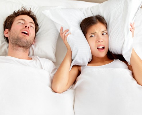 Man snoring with woman using pillow over ears